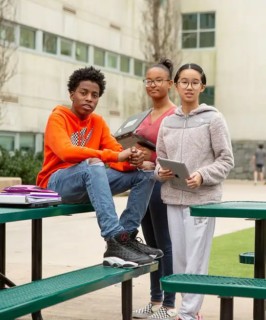 Students outside school at picnic table with books and laptop computers