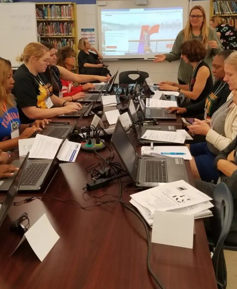 Teachers in a meeting at a long desk while each using a laptop computer